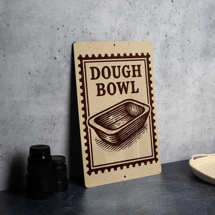 A sign for a dough bowl is displayed on a table, with a stack of black containers and a white dish visible to the side.