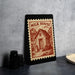 a framed stamp-like design with a house illustration, placed on a table next to some black camera lenses.