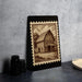 a wooden barn with a porch, depicted on a black frame with a decorative border.