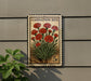 A vintage-style stamp featuring a vibrant image of red carnation flowers, mounted on a wall next to a plant.