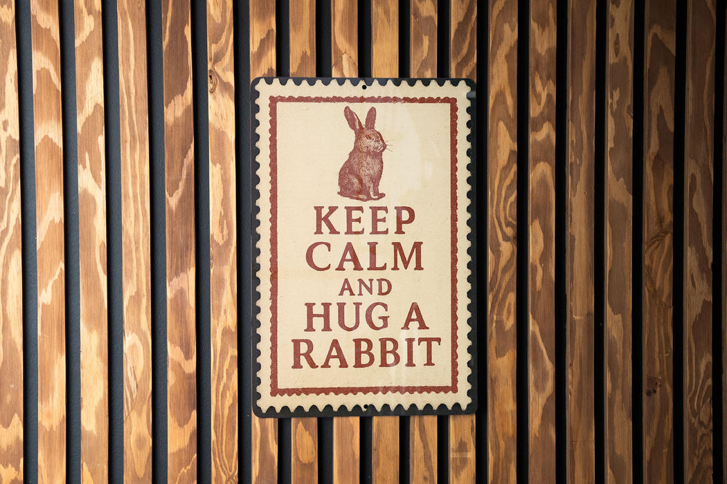 A sign with the message "KEEP CALM AND HUG A RABBIT" is displayed on a wooden wall.
