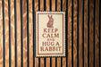 A sign with the message "KEEP CALM AND HUG A RABBIT" is displayed on a wooden wall.