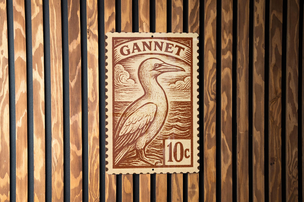 A brown postage stamp featuring a bird, likely a gannet, is displayed on a wooden wall.