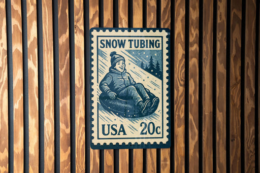 A blue and white postage stamp featuring a person riding a snow tube, mounted on a wooden wall.