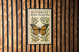 A framed poster with a butterfly and host plants is displayed on a wooden wall.