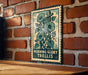 A metal sign with a floral design is mounted on a brick wall.