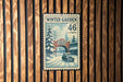 A vintage-style postage stamp depicting a snowy winter scene with a car and a building, mounted on a wooden wall.