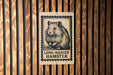 a wooden wall with a rectangular sign featuring a hamster illustration and the text "LONG HAIRED HAMSTER" printed on it.