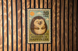 A 20 US postage stamp featuring a smiling hedgehog, with the text "HEDGEHOG HAPPINESS" printed on it.
