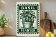 a potted basil plant with a green and white stamp-like design, placed on a wooden surface next to a wooden cutting board and some lemons.