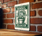 A metal sign with a green border and a picture of a basil plant in a pot, mounted on a brick wall.