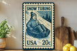 A vintage-style snow tubing postage stamp from the United States, featuring a smiling child in a snow tube.