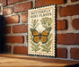 A metal sign with a butterfly and host plants is mounted on a brick wall.