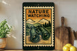 A vintage-style metal sign with a nature-themed illustration, featuring a pair of binoculars, is displayed on a shelf next to a wooden cutting board and a potted plant.