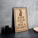 A metal sign with a rabbit illustration and the text "KEEP CALM AND HUG A RABBIT" is displayed on a table.