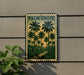 A framed vintage-style poster of palm trees is displayed on a wall, with a plant to the left.