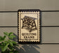 a sign that reads "QUILTING FRAME" with a decorative border, mounted on a wall next to a plant.