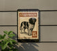 A stamp-like sign featuring a black and white dog illustration, mounted on a wall.