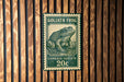 A postage stamp featuring a detailed illustration of a Goliath Frog, which is a type of frog. The stamp is mounted on a wooden wall.