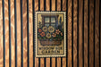 A metal sign with a floral design hangs on a wooden wall, displaying the text "WINDOW BOX GARDEN".
