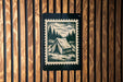 A black and white illustration of a tent is displayed on a wooden wall, with a black border around it.