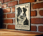 A metal sign featuring a black and white illustration of a Welsh sheepdog, mounted on a brick wall.