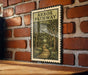A framed illustration of a forest path, mounted on a brick wall.