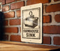 A sign with a drawing of a farmhouse sink mounted on a brick wall.