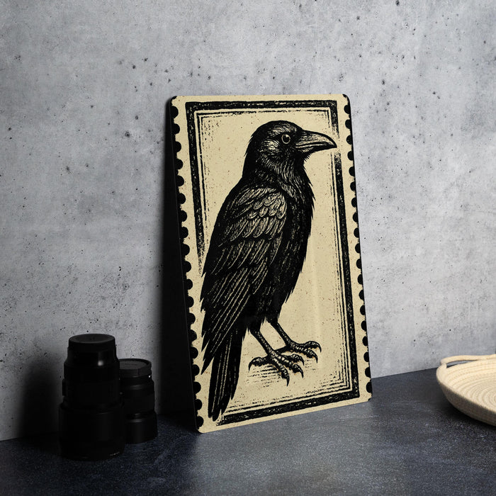 a framed illustration of a black crow on a beige background, placed on a countertop next to some black camera lenses.