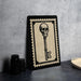 a framed key with a skull on it, placed on a countertop next to some black camera lenses.