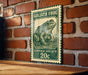 A green and white postage stamp featuring a detailed illustration of a frog, mounted on a brick wall.
