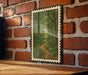 A framed painting of a forest path is hanging on a brick wall, with a wooden table below it.