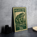 A green and beige postage stamp featuring a detailed illustration of a frog, placed on a gray countertop next to some black camera lenses.