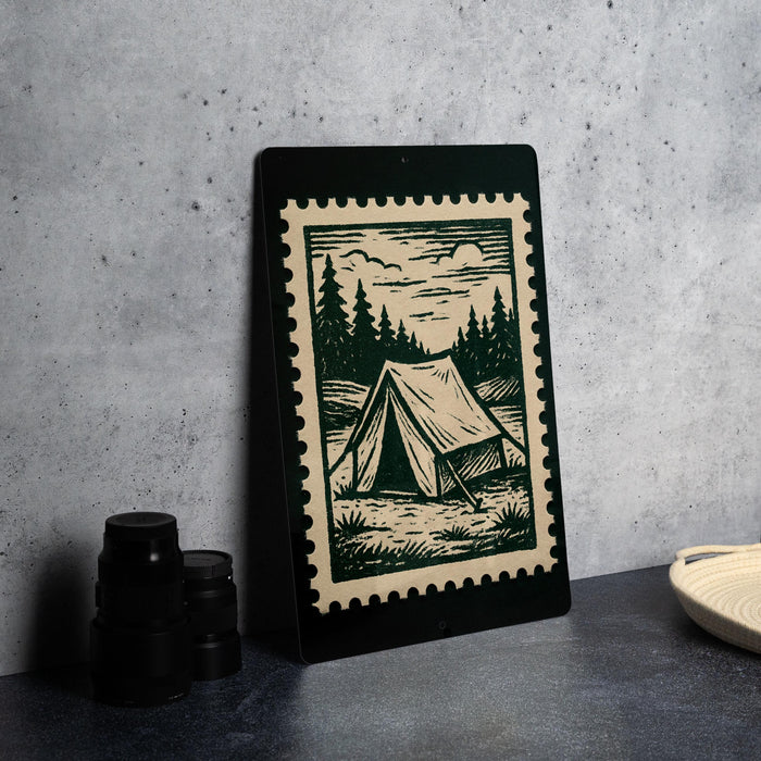 A framed print depicting a tent in a forest setting is displayed on a table, accompanied by a stack of black camera lenses and a woven basket.
