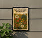 a framed poster of a wildflower meadow, with a border and decorative elements, hanging on a wall.