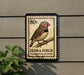 A postage stamp featuring a colorful illustration of a zebra finch perched on a branch.