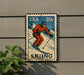 A vintage-style metal sign featuring a skier in an orange outfit, mounted on a wall.