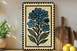 a decorative tile with a blue flower design, placed on a wooden surface next to a wooden cutting board and a potted plant.