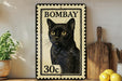 A vintage-style stamp depicting a black cat, with the text "BOMBAY 30c" printed on it. The stamp is placed on a shelf next to a wooden cutting board and a potted plant.