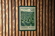 A green and white postage stamp with a maze design, mounted on a wooden wall.