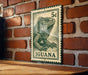 A green and white postage stamp featuring an illustration of an iguana is displayed on a brick wall.