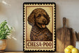 A framed image of a brown dog with curly fur, labeled "CHESA-POO", is displayed on a shelf next to a wooden cutting board and a potted plant.