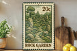 A metal sign with a landscape illustration depicting a rock garden, placed on a wooden shelf next to a wooden cutting board and a potted plant.