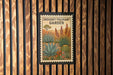 a poster of a desert garden with a cactus and other desert plants, hanging on a wooden wall.