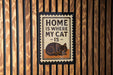 A sign with the text "HOME IS WHERE MY CAT IS" and an illustration of a cat is mounted on a wooden wall.