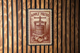 a wooden wall with a vintage-style stamp or sign that reads "APPLE PRESS" and depicts a wooden press machine with apples.