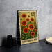 A metal stamp with a floral design and the text "GAILLARDIA BED" printed on it, placed on a gray surface next to some black camera lenses.