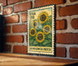 A vintage-style metal stamp depicting a field of sunflowers, mounted on a brick wall.