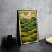 a framed painting of a countryside landscape with rolling hills and trees, placed on a table next to some black camera lenses.