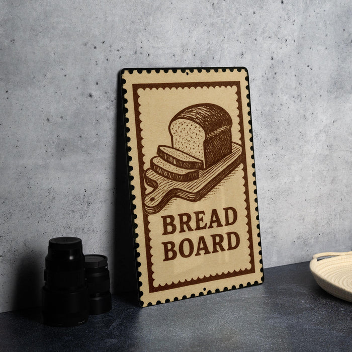 A wooden sign with a loaf of bread on it, placed on a countertop next to some black containers.